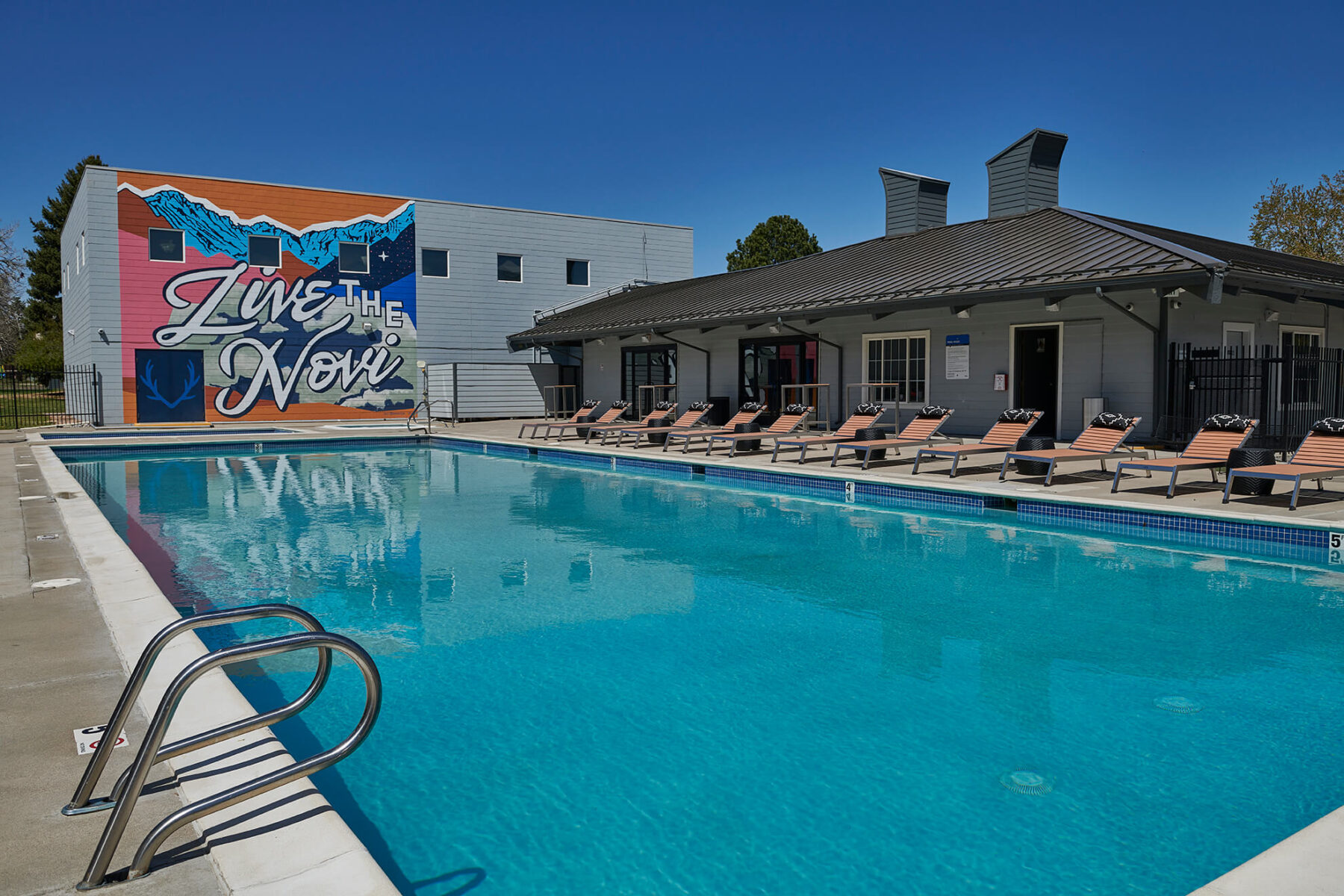 wide view of the pool and lounge poolside chairs with the colorful mural on the wall